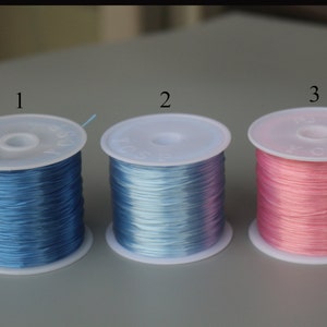 Peut inclure: Trois bobines de fil &eacute;lastique, une bleue, une bleu clair et une rose.
