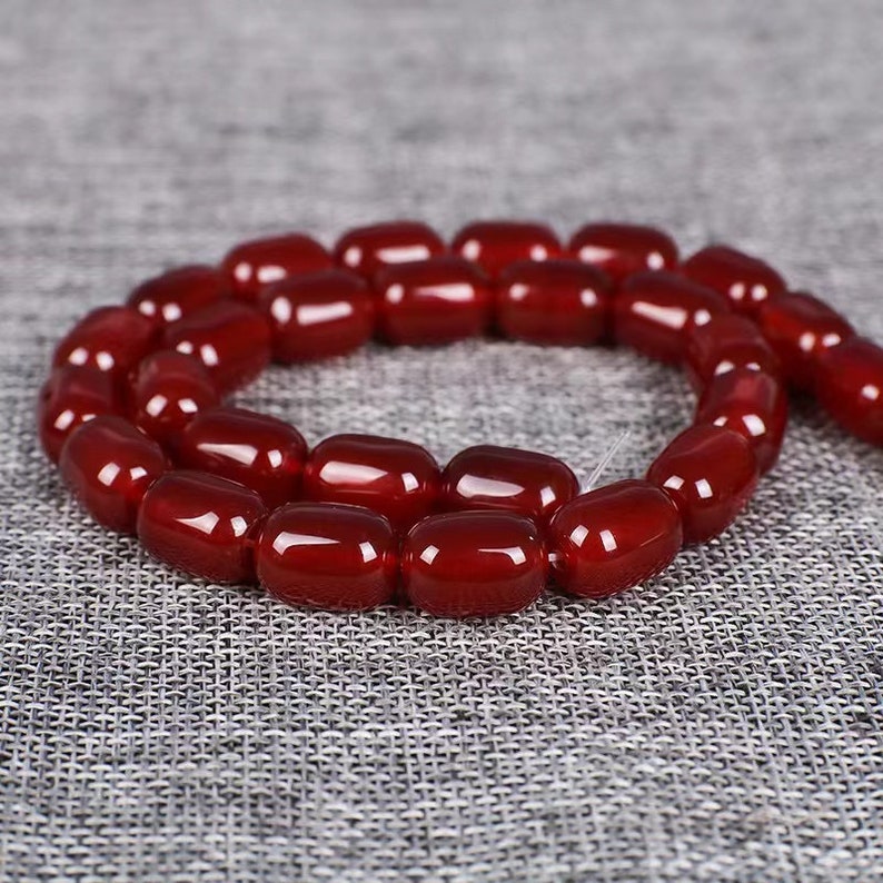 May include: A strand of red carnelian beads, each bead is a smooth, oval shape.