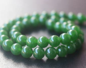 May include: A strand of green jade beads, each bead is round and smooth. The beads are strung together on a clear thread.