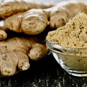May include: Close-up of fresh ginger root and ground ginger powder in a glass bowl. The ginger root is light brown and has a knobby texture. The ground ginger powder is a light beige color and has a fine texture.