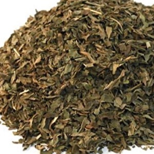May include: Dried green herbs, such as parsley or basil, are piled in a heap. The herbs are finely chopped and ready to be used in cooking.