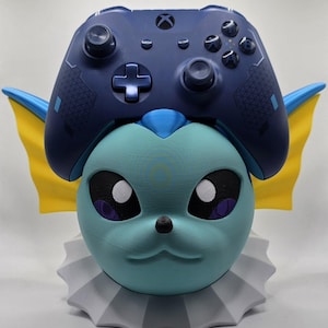 May include: A blue and yellow 3D printed Pokemon Vaporeon controller stand. The stand is designed to hold a blue Xbox controller.