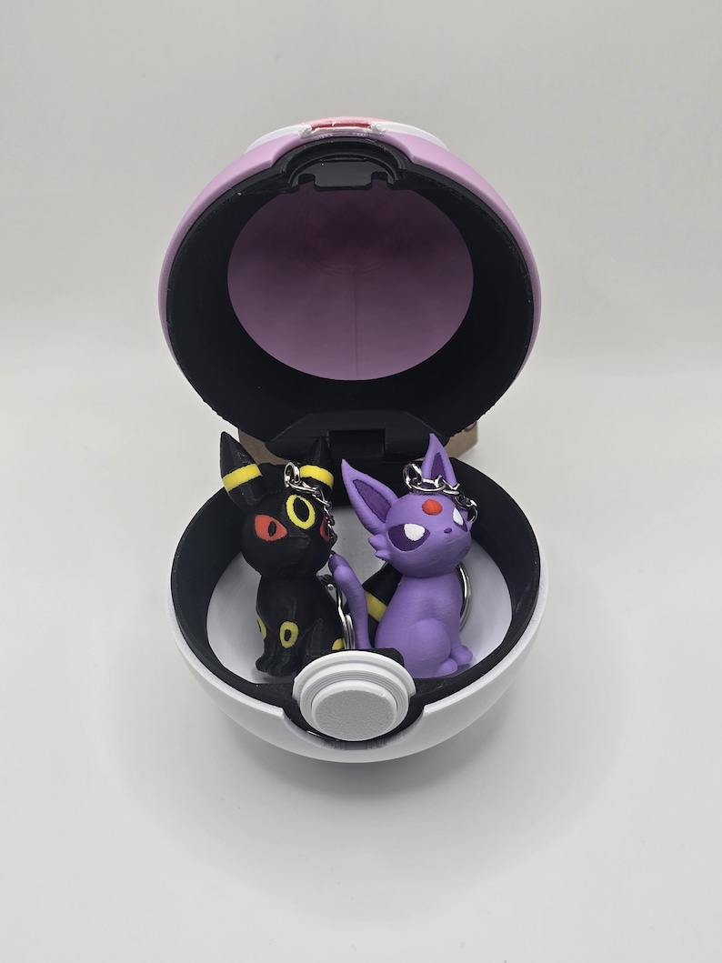 May include: A white and purple Poke Ball keychain with a black and yellow Umbreon and a purple Espeon figurine inside.