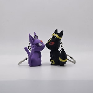May include: A purple and black cartoon character keychain set. The characters are facing each other and appear to be kissing. The keychain is made of plastic and has a silver metal ring.