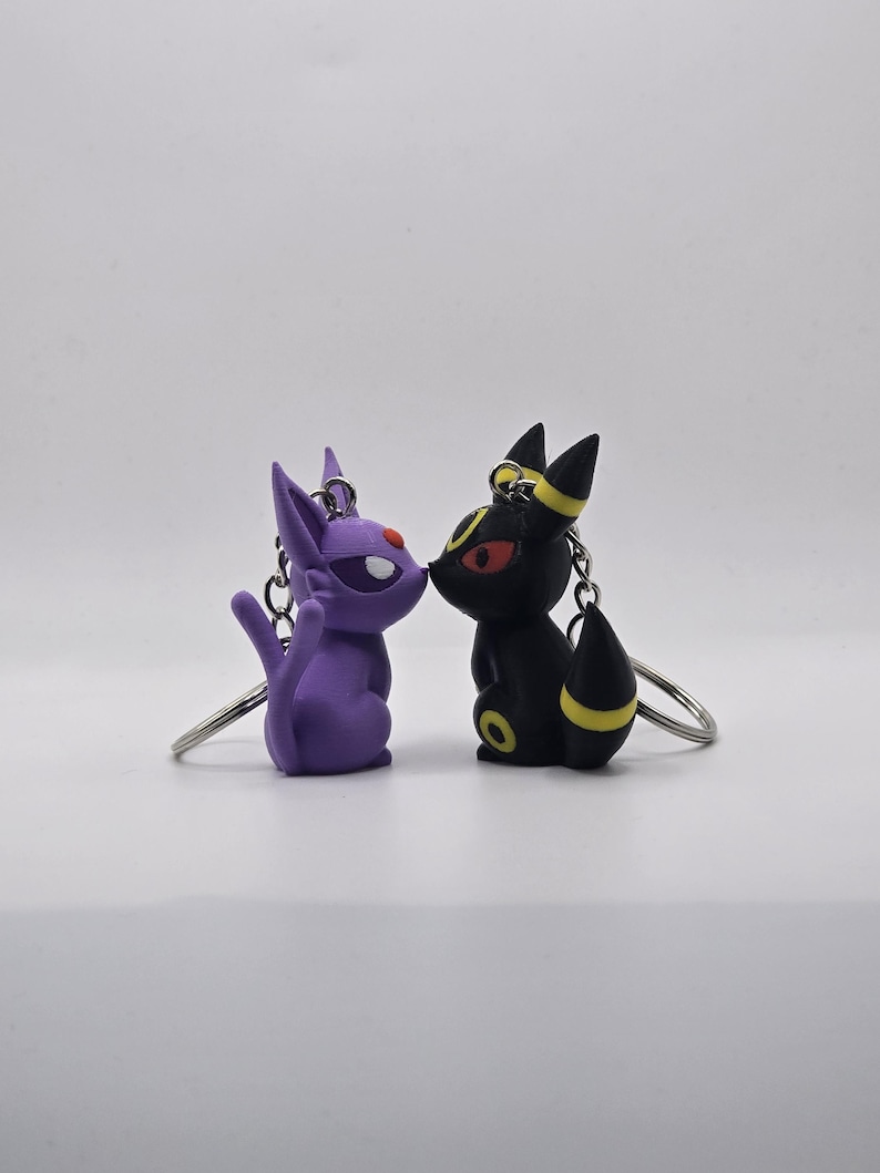 May include: A purple and black cartoon character keychain set. The characters are facing each other and appear to be kissing. The keychain is made of plastic and has a silver metal ring.