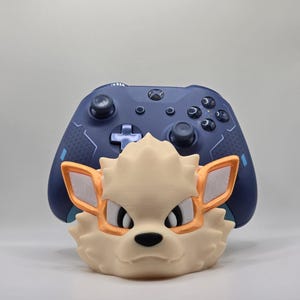May include: A 3D printed stand for a video game controller, shaped like the head of a cartoon fox with orange ears and a white face.