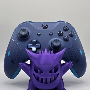 May include: A purple Gengar figurine standing in front of a blue Xbox controller.