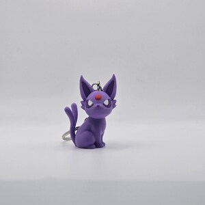 May include: Purple and red Pokemon keychain featuring a cartoon cat-like character with a red eye.