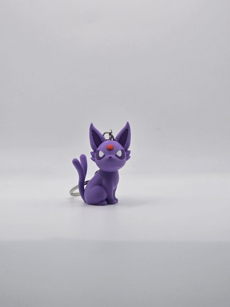 May include: Purple and red Pokemon keychain featuring a cartoon cat-like character with a red eye.