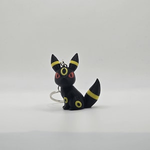 May include: Black and yellow Pokemon keychain featuring a sitting Umbreon with red eyes.