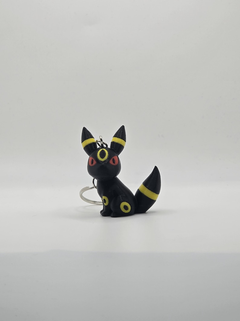 May include: Black and yellow Pokemon keychain featuring a sitting Umbreon with red eyes.