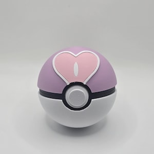 May include: A pink and white Poke Ball with a heart-shaped design on the top. The heart is pink with a white outline.