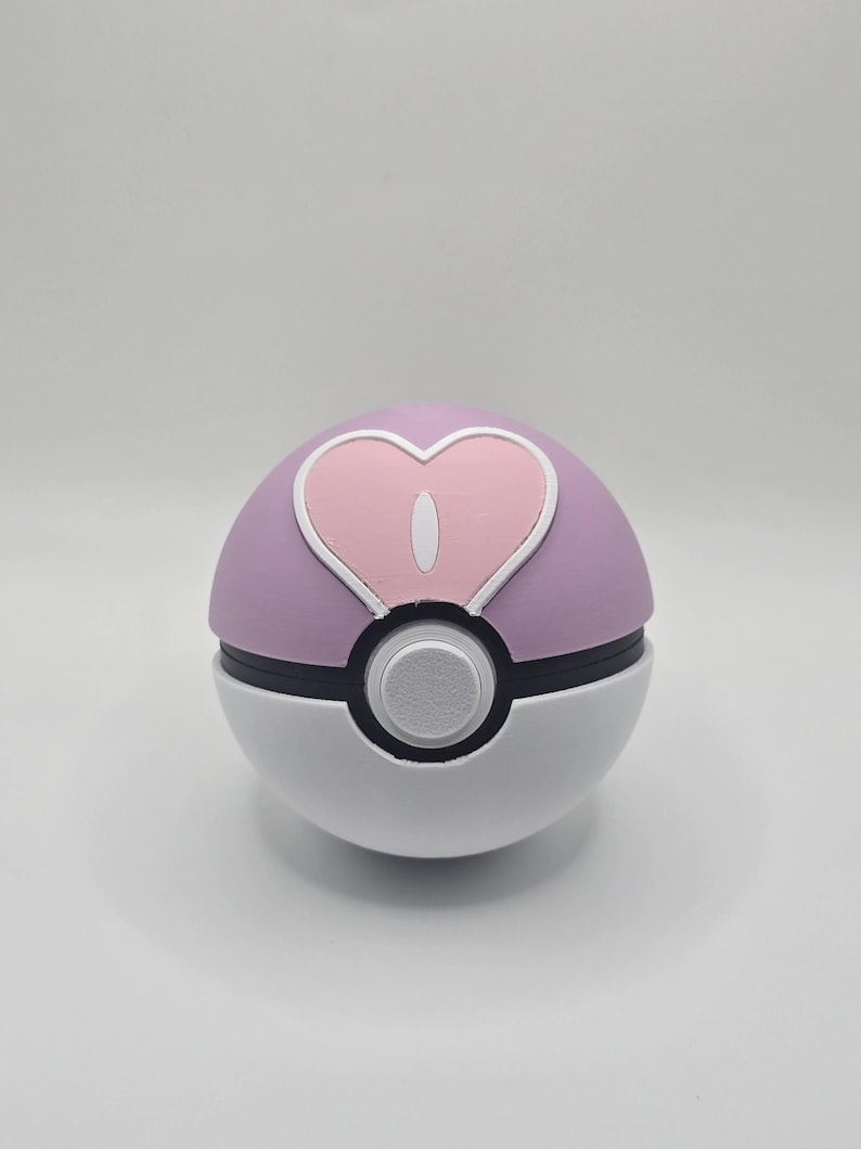 May include: A pink and white Poke Ball with a heart-shaped design on the top. The heart is pink with a white outline.