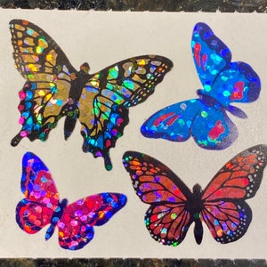 May include: Four colorful butterfly stickers with iridescent, glittery wings. The butterflies are in shades of gold, blue, red, and orange. The stickers are on a white background.