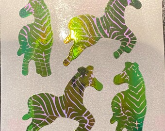 May include: Four holographic zebra stickers in various poses. The stickers have a green and gold iridescent finish with pink and purple stripes. The stickers are on a white background.