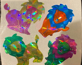 May include: Four holographic stickers of cartoon lions in various colors: purple, orange, green, and pink. Each lion has a geometric, faceted design, creating a shimmering effect. The stickers are on a white background.