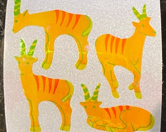 May include: Four stickers featuring stylized yellow and orange antelope-like creatures with green horns and accents. The stickers have a holographic, iridescent finish, and are arranged in different poses, including standing and lying down.