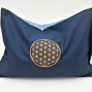 Puede incluir: Una almohada azul con un diseño de flor de la vida bordado en oro.