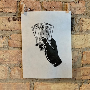 May include: Black and white print of a hand holding a set of playing cards. The cards are a 5 of spades, a 5 of diamonds, a jack of hearts, and a queen of hearts.
