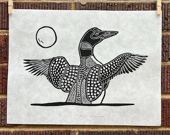 May include: Black and white line art print of a loon with its wings spread wide. The loon is stylized with a geometric pattern and a circle representing the moon is in the background.