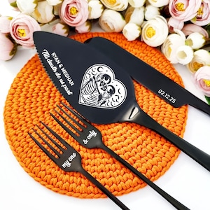 Op de afbeelding: Zwarte bruidstaartmes en twee vorken met gegraveerde tekst. Het mes heeft een hartvormig ontwerp met een skeletpaar erin. De tekst op het mes luidt "Ryan & Meghan Till death do us part 02.12.25". De vorken hebben de tekst "my one & only" gegraveerd.