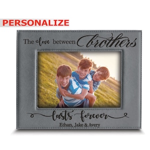 May include: A gray leather photo frame with the text "The love between brothers lasts forever" and the names "Ethan, Jake & Avery" engraved on the bottom. The frame has a picture of three brothers smiling and hugging.