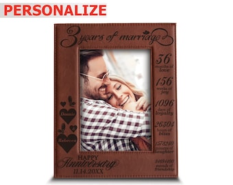May include: A brown leather photo frame with a picture of a couple inside. The frame is engraved with the text "3 years of marriage" and a list of time measurements, including months, weeks, days, hours, minutes, and seconds. The names "Donnie" and "Rebecca" are also engraved on the frame, along with the text "Happy Anniversary 11.14.20XX".
