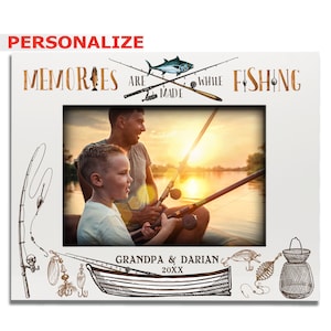 May include: A white photo frame with a fishing theme. The frame has a picture of a man and a boy fishing on a lake. The text "Memories are made while fishing" is at the top of the frame. The text "Grandpa & Darian 20XX" is at the bottom of the frame.