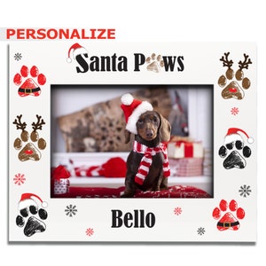 May include: White photo frame with a red and white Santa hat on a paw print, the text "Santa Paws" and the name "Bello" in black text. The frame has a brown and white dachshund wearing a red Santa hat and a red and white scarf in the center.