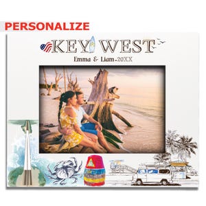 May include: White picture frame with a photo of a couple on a beach. The frame has the words "KEY WEST" and "Emma & Liam - 20XX" printed on it. The frame also has illustrations of a crab, a colorful buoy, and a van.