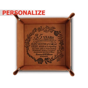 May include: A brown leather catchall tray with a personalized inscription commemorating a 35th anniversary. The inscription reads "35 Years Anniversary 420 Months of Love 1826 Weeks of Loyalty 12785 Days of Friendship 306840 Hours of Laughter 18410400 Minutes of Bliss Emma William 10/22/20XX".