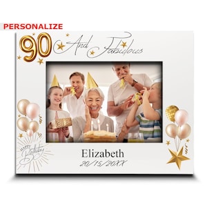 May include: A white photo frame with a gold 90 and stars. The text "And Fabulous" is written in black cursive. The frame has a photo of a family celebrating a birthday. The text "Happy Birthday" is written in gold cursive. The text "Elizabeth 20/15/20XX" is written in black cursive.