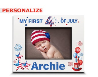 Puede incluir: Marco de fotos blanco con un tema patriótico rojo, blanco y azul. El marco tiene una foto de un bebé durmiendo con un gorro rojo, blanco y azul. El texto "My First 4th of July" está en la parte superior del marco. El texto "Archie" está en la parte inferior del marco.