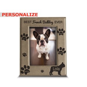 May include: A brown leather photo frame with a picture of a French Bulldog. The frame has the text "BEST French Bulldog EVER" at the top and the words "LIVELY", "PLAYFUL", "SMART", and "MOBILE" around the picture. The dog's name "Lola" is written below the picture.