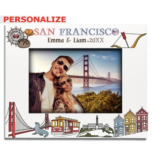 May include: Personalized photo frame with a white background and a picture of a couple in front of the Golden Gate Bridge. The frame has a red, white, and blue American flag, a red cable car, a sea lion, and a lighthouse. The text "SAN FRANCISCO" is at the top of the frame, and the text "Emma & Liam-20XX" is below it.