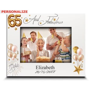 May include: A white photo frame with a gold border and a gold number 65, the words "And Fabulous" and stars. The frame has a photo of a family celebrating a birthday with a cake and balloons. The text "Elizabeth 20/15/20XX" is at the bottom of the frame.