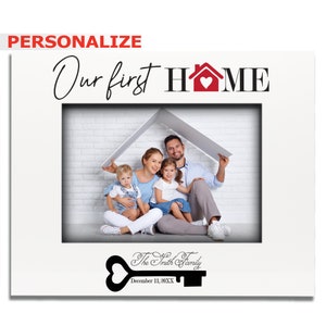 May include: White photo frame with a red house icon and the text "Our first HOME". The frame has a photo of a family of four sitting under a white roof. The text "The Smith Family" and "December 11, 20XX" is below the photo.