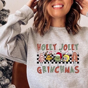 May include: A gray sweatshirt with the text "Holly Jolly Grinchmas" and a graphic of cartoon characters holding candy canes. The characters include the Grinch, Cindy Lou Who, and a gingerbread man.