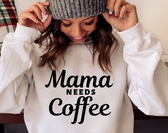 Pode incluir: Camisola branca com texto preto que diz "Mama Needs Coffee".