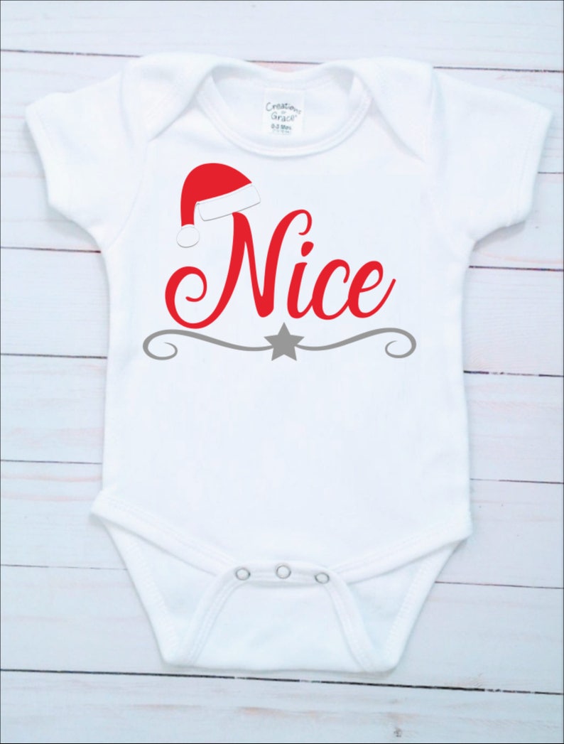 May include: White baby bodysuit with a red Santa hat and the word "Nice" in red script. A gray star and decorative line are below the word. The bodysuit has short sleeves and snaps at the bottom.