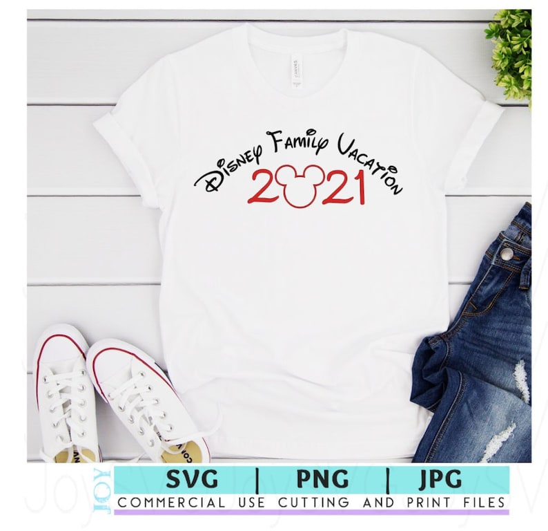 May include: White t-shirt with black text that reads "Disney Family Vacation 2021" with a red Mickey Mouse head in between the numbers. The shirt is laying on a white wooden surface with a pair of white sneakers and blue jeans.