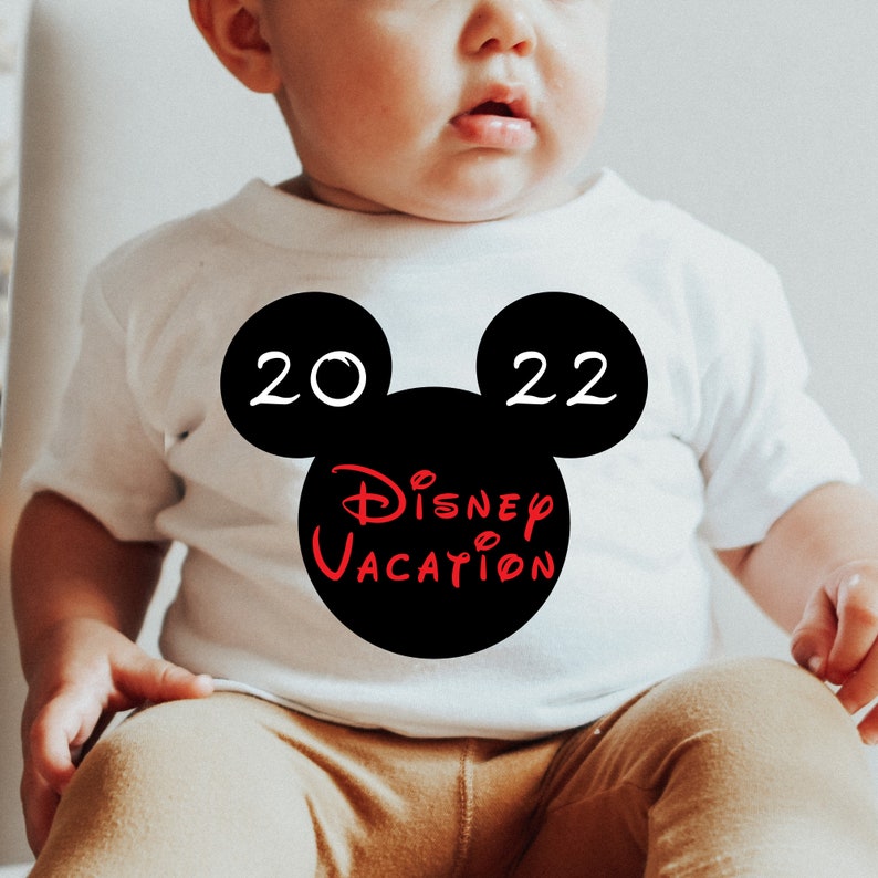 May include: A white baby onesie with a black Mickey Mouse head design. The Mickey Mouse head has the numbers 20 and 22 on the ears and the words "Disney Vacation" inside the head.