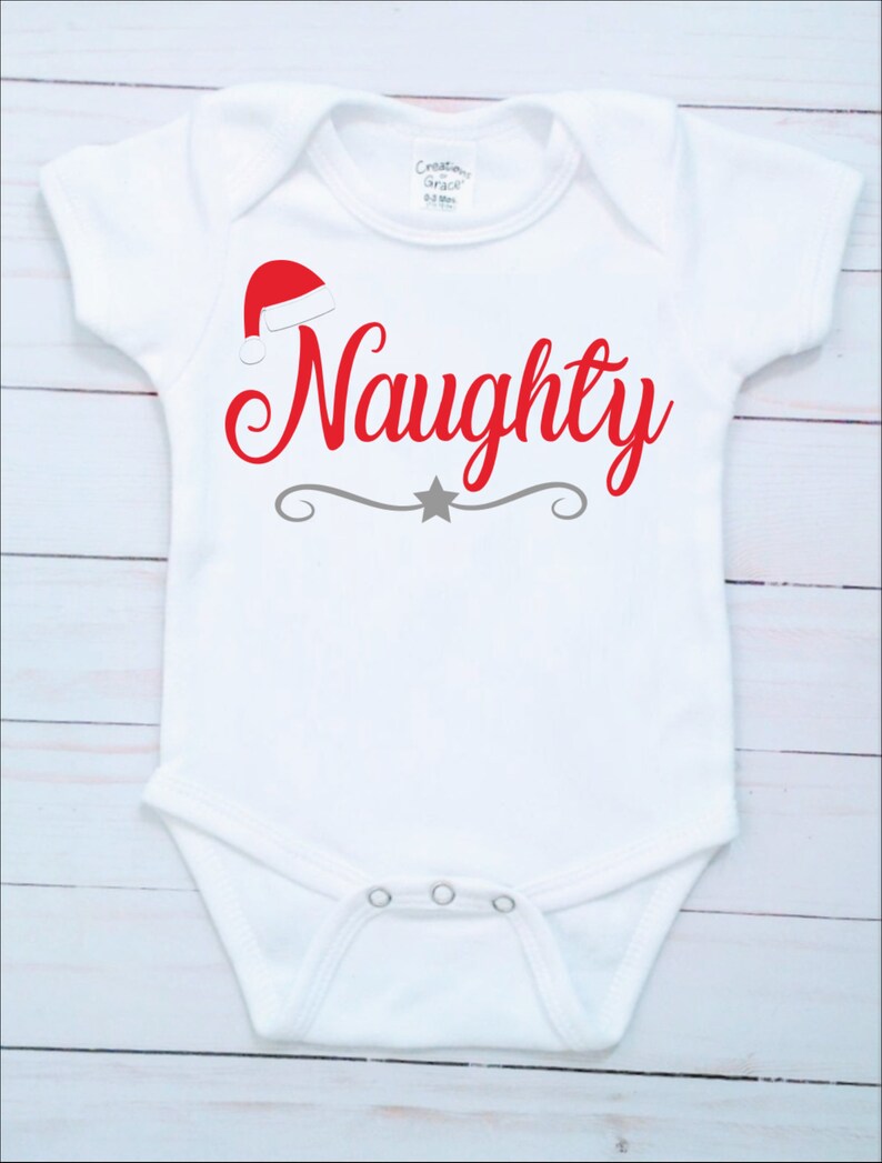 May include: White baby onesie with a red Santa hat and the word "Naughty" in red script. A gray decorative line with a star is below the word. The onesie has short sleeves and snap closures.