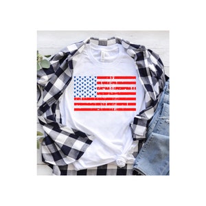 May include: White t-shirt featuring a red, white and blue American flag design. The flag is distressed and has blue Mickey Mouse heads in the blue field.