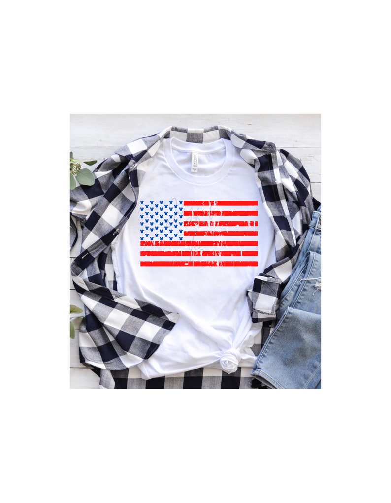 May include: White t-shirt featuring a red, white and blue American flag design. The flag is distressed and has blue Mickey Mouse heads in the blue field.
