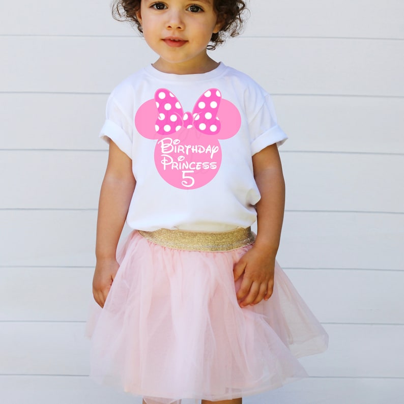 May include: A white t-shirt with a pink Minnie Mouse head design featuring white polka dots. The shirt says "Birthday Princess 5" in pink letters.