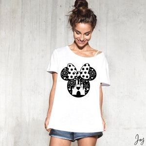 May include: White t-shirt with a black and white graphic of Mickey Mouse ears with a bow and a castle inside. The bow is polka dotted.