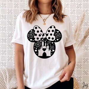 May include: White t-shirt with a black silhouette of Mickey Mouse ears with a bow and a castle inside. The bow has white polka dots and the castle has fireworks and hearts around it.