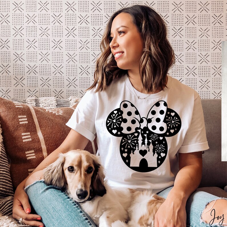 May include: A white t-shirt with a black and white graphic of Minnie Mouse ears with a bow and fireworks. The graphic also includes a black silhouette of Cinderella's castle.