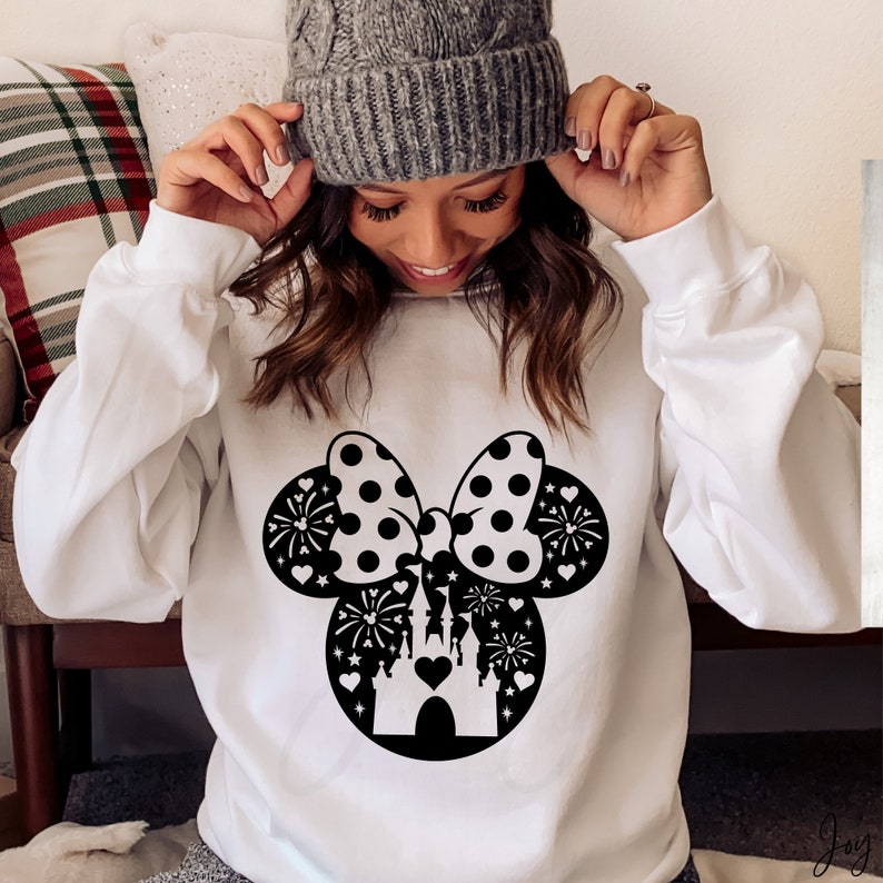 May include: White sweatshirt with a black and white Minnie Mouse head design. The design features a bow with polka dots, a castle, and fireworks.